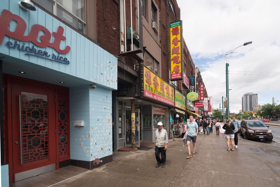 People walking along a city sidewalk in front of colorful Asian restaurant signs