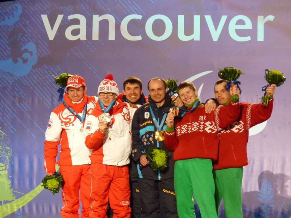 Six athletes holding bouquet flowers pose together on a podium in front of a Vancouver sign.