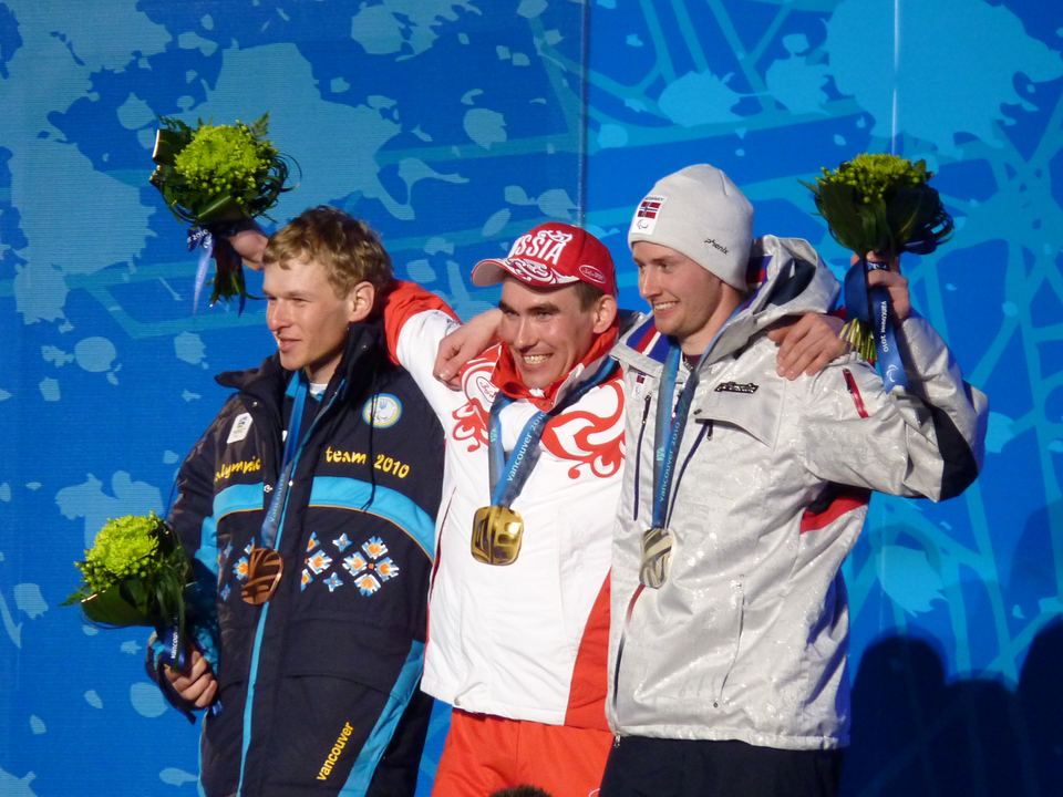 Three athletes wearing winter jackets and medals smile on the podium.