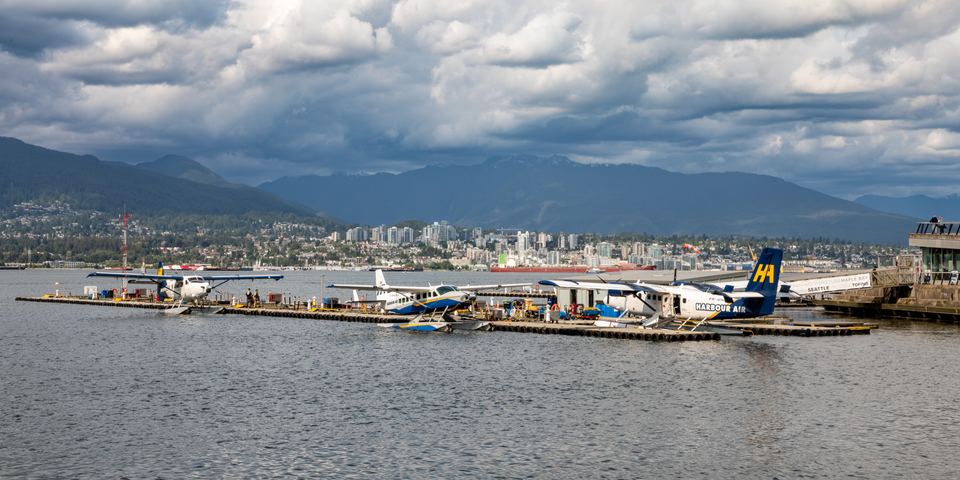 Several floatplanes tied to a dock on Vancouver harbor with mountains behind.