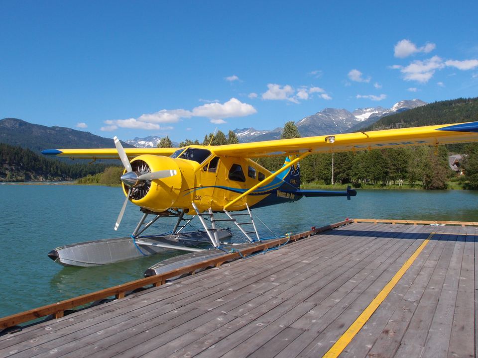 A yellow seaplane docked on calm water with mountains under a blue sky.