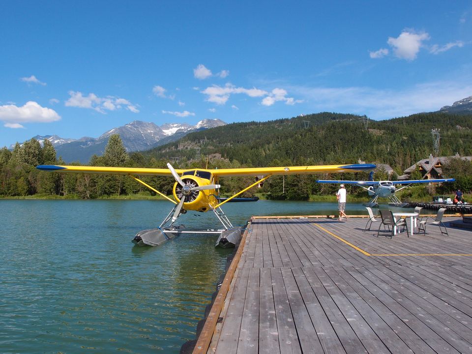 A wooden pier extending into green water with a yellow floatplane docked beside it.