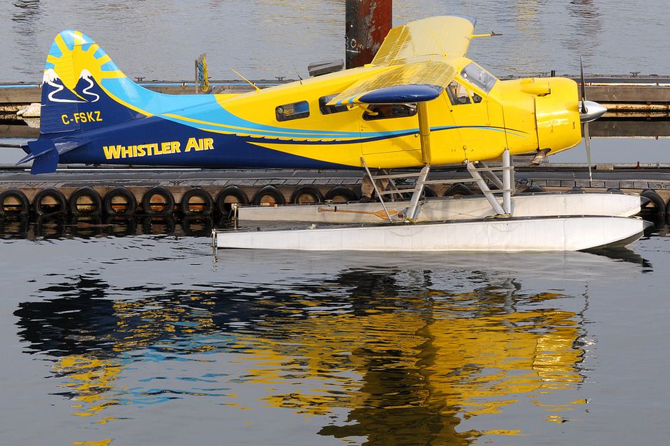 A bright yellow and blue floatplane docked on reflective water