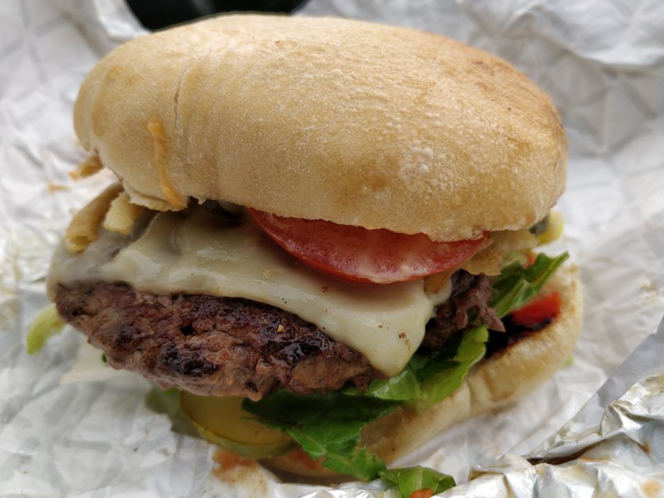 A freshly prepared cheeseburger with tomato and lettuce in foil wrapping.