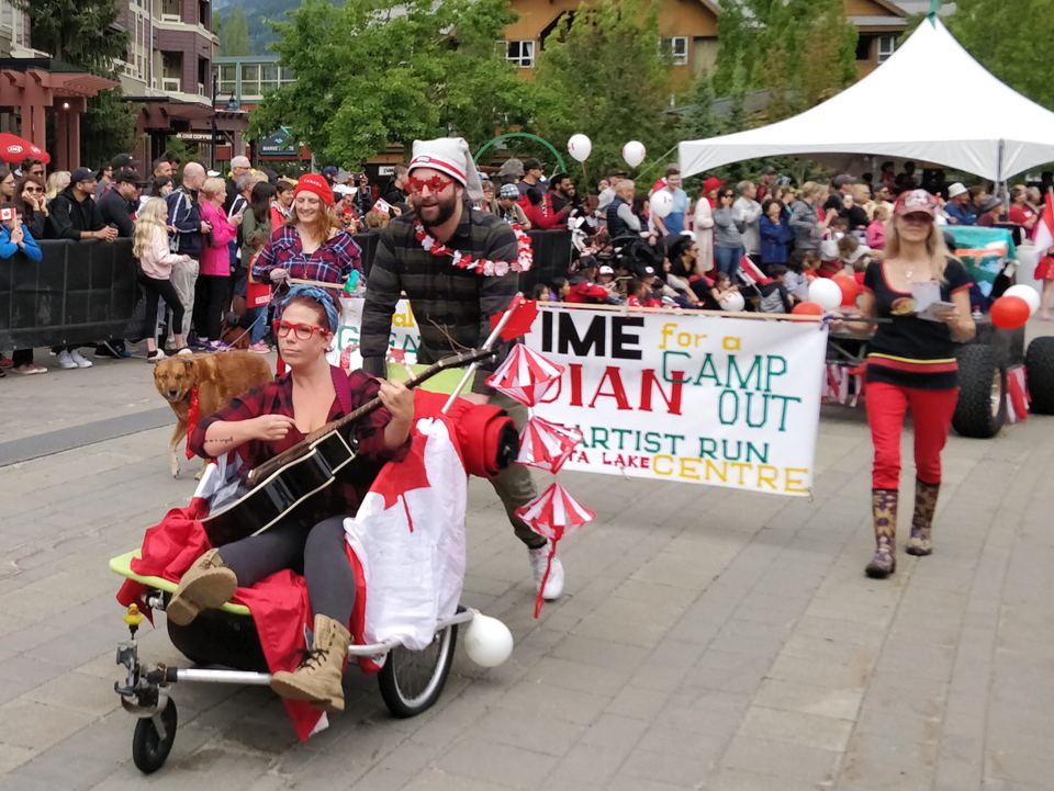 A crowd of people watching a parade float with a woman playing guitar in Whistler Village.