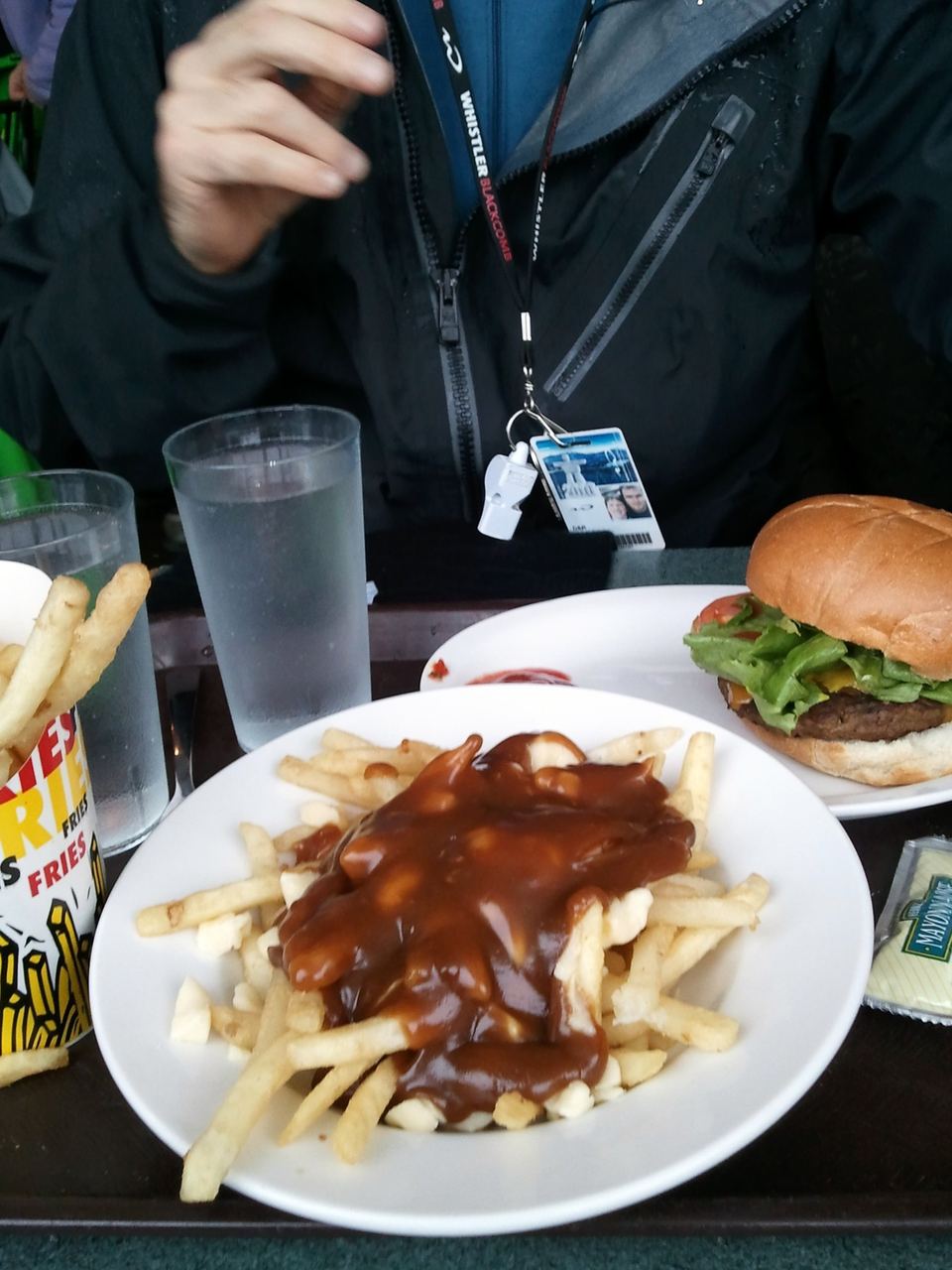 A plate of poutine with gravy and cheese curds next to a burger and fries