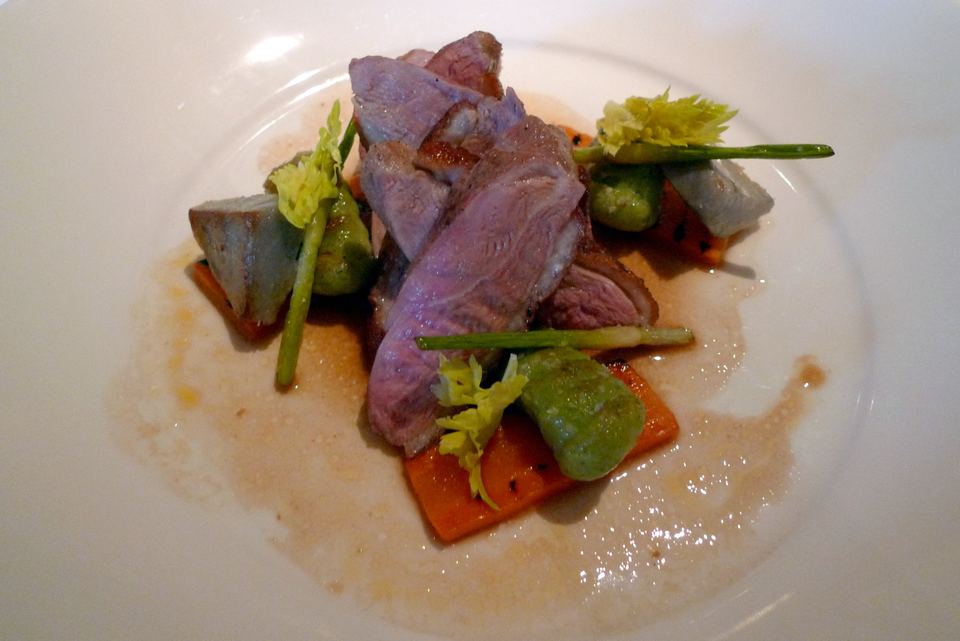Plated duck breast garnished with vegetables and herbs on a white plate