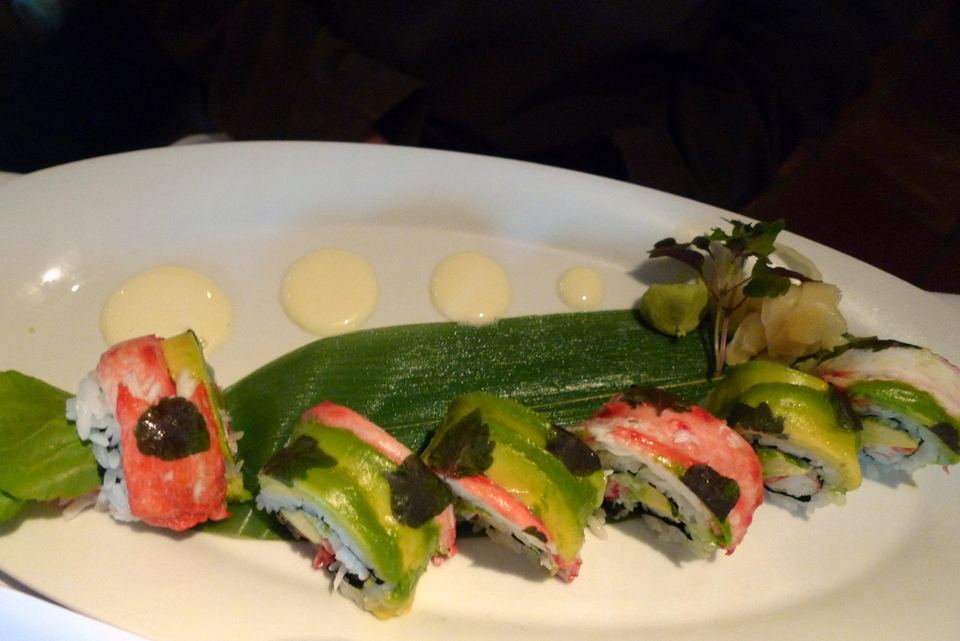 A white platter featuring sushi rolls topped with sliced avocado