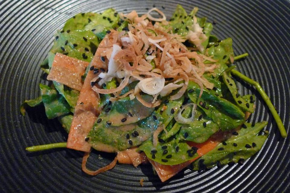 Fresh spinach salad with sesame seeds and crispy shallots on a dark dish