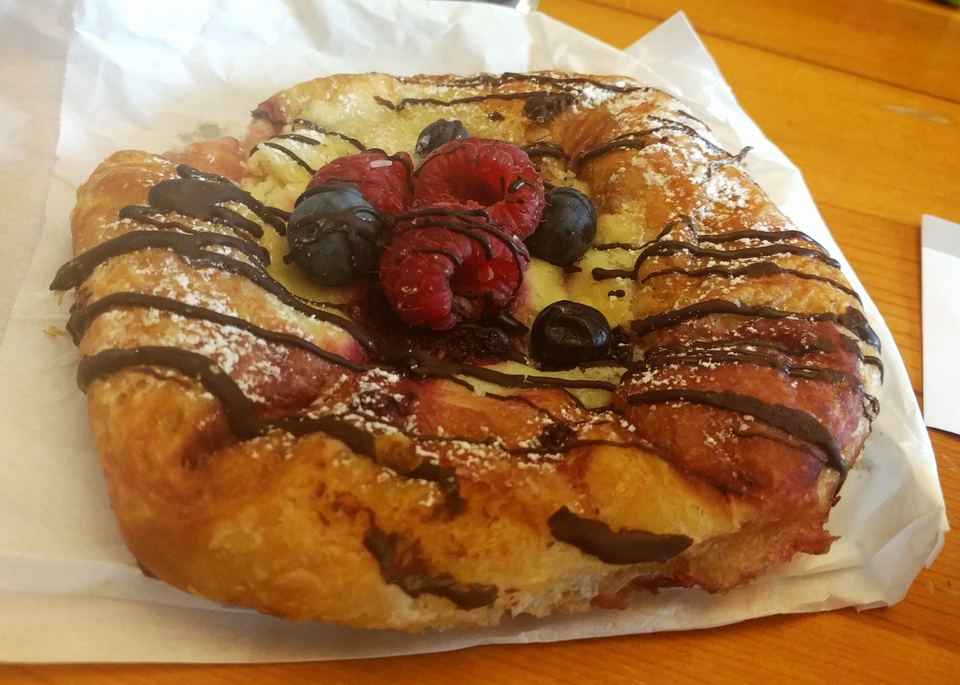 A baked pastry topped with fresh raspberries, blueberries, powdered sugar, and chocolate drizzle.