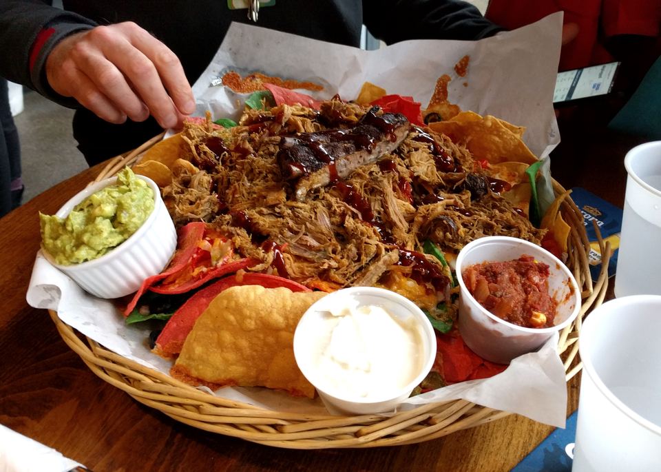 A large basket of loaded tortilla chips topped with barbecue pulled pork and dipping sauces