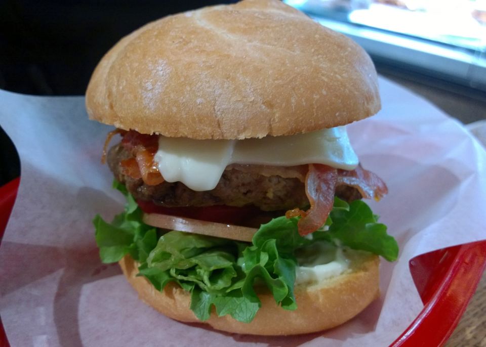 Close up view of a bacon cheeseburger with lettuce and tomato in a basket