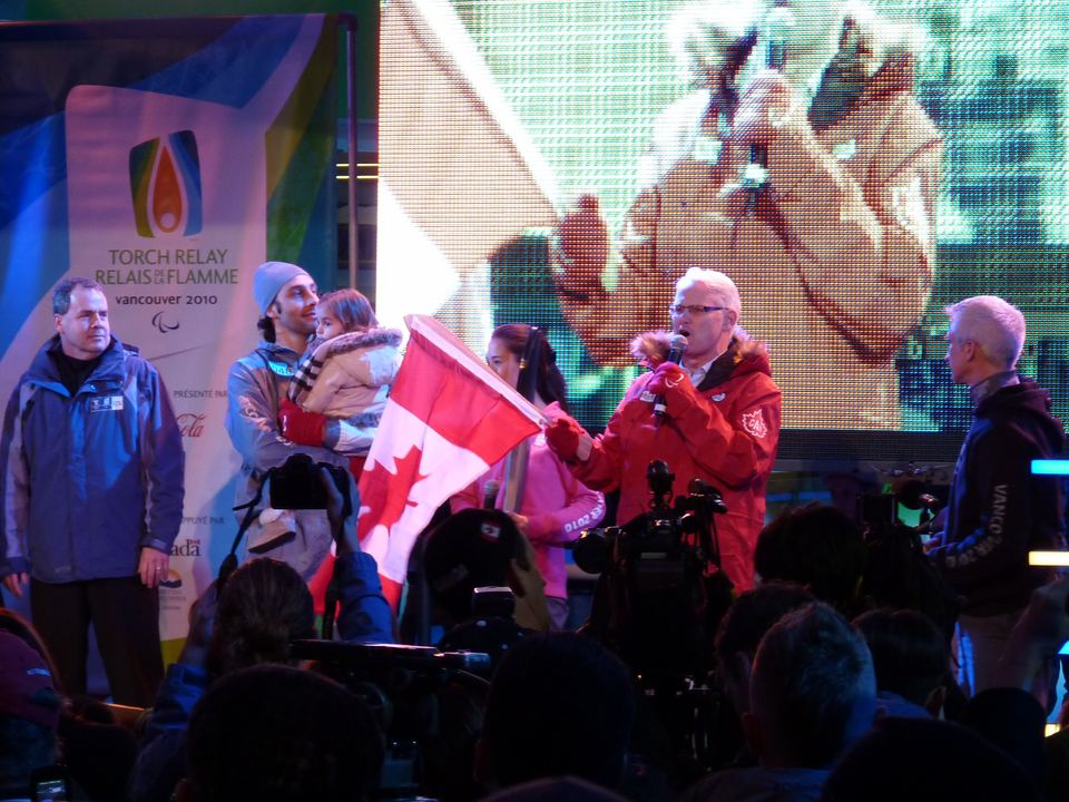 A group of people on stage holding a Canadian flag during an evening event.