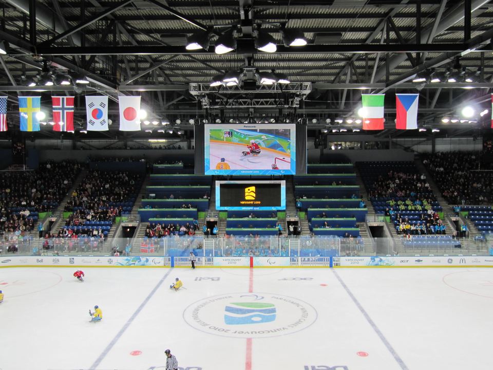 Wide interior shot of an indoor ice hockey arena with flags and seating.