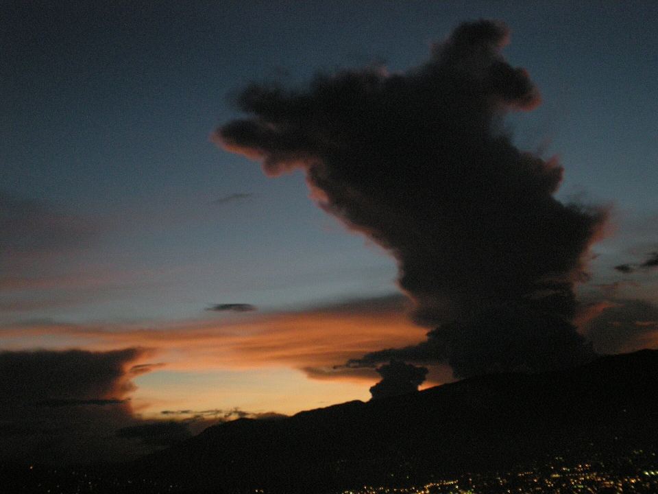 Dark mountain silhouette at sunset with glowing orange horizon and dramatic dark clouds above.