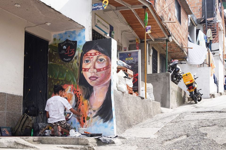 A street artist painting a large portrait mural on a house wall in Comuna 13, Medellin