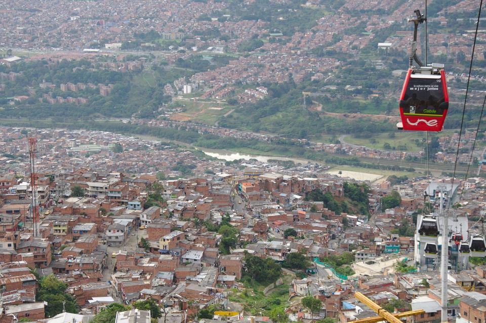 A red Metrocable gondola crossing high above the red-brick neighbourhoods of Medellin