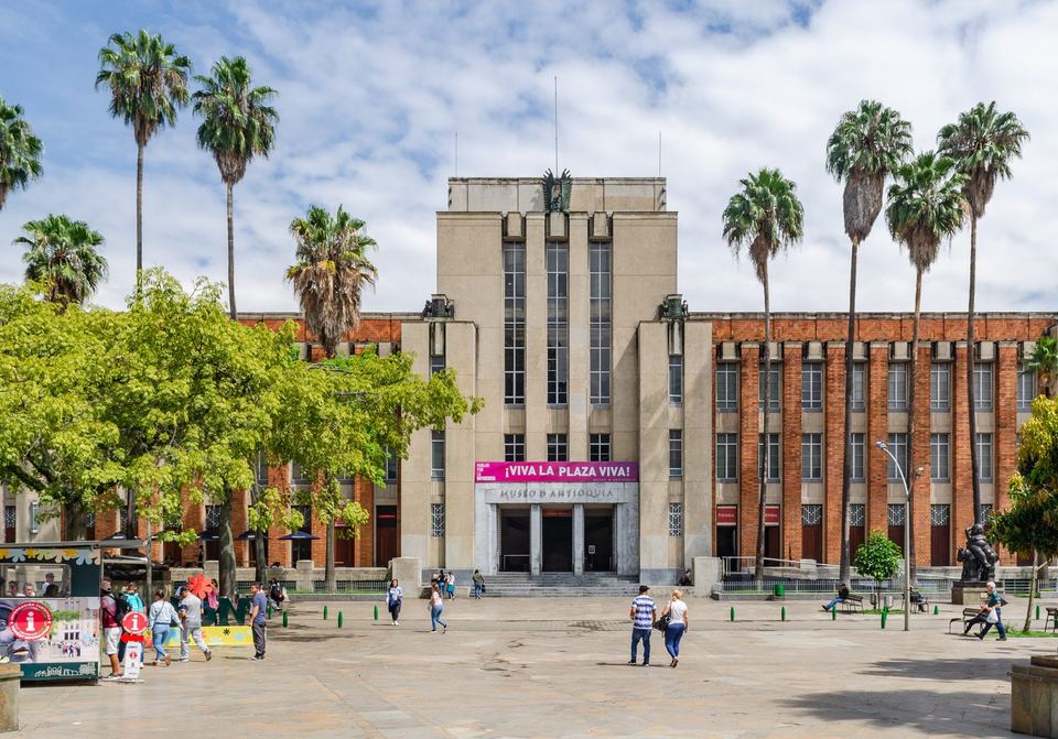 The facade of the Museo de Antioquia behind palm trees on Plaza Botero