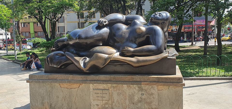 Bronze sculpture of a reclining voluptuous woman on a stone pedestal in Plaza Botero.