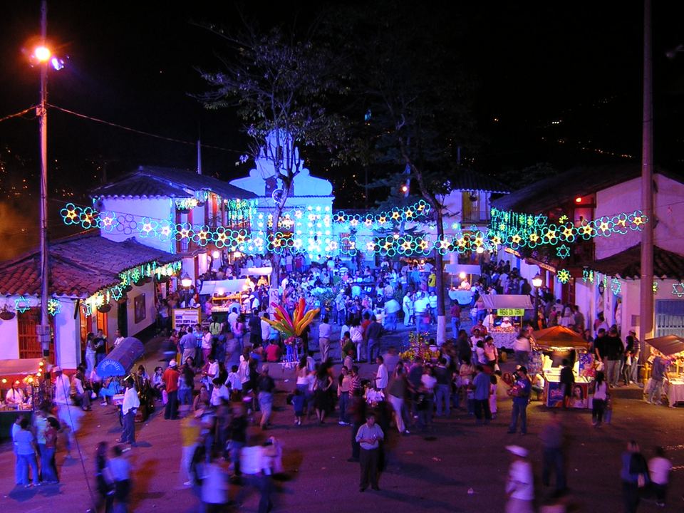 Crowds gathering in an illuminated plaza surrounded by traditional white buildings at night.