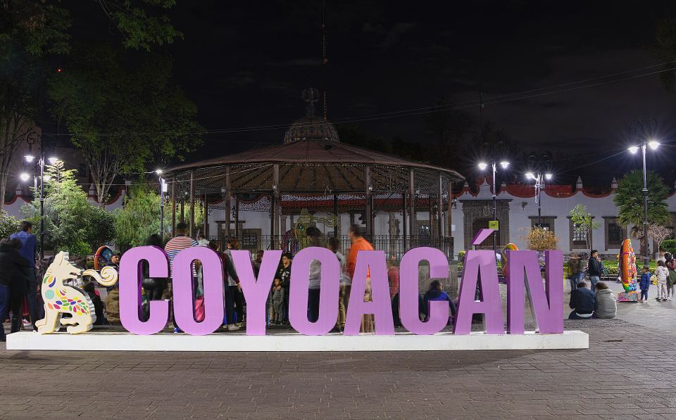 Large purple letters spelling COYOACAN illuminated in a town square at night.