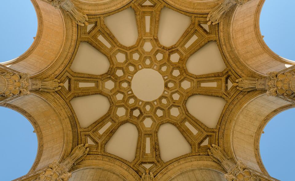 Symmetrical view looking straight up into an intricate geometric stone dome.