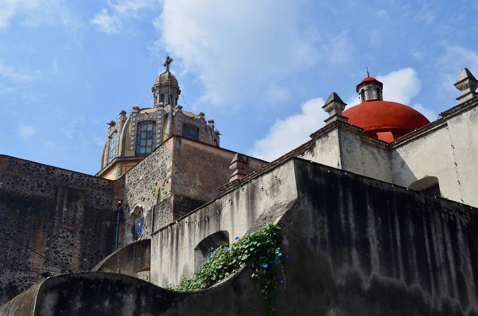 Low-angle view of an old stone church featuring a bright red dome against blue sky.