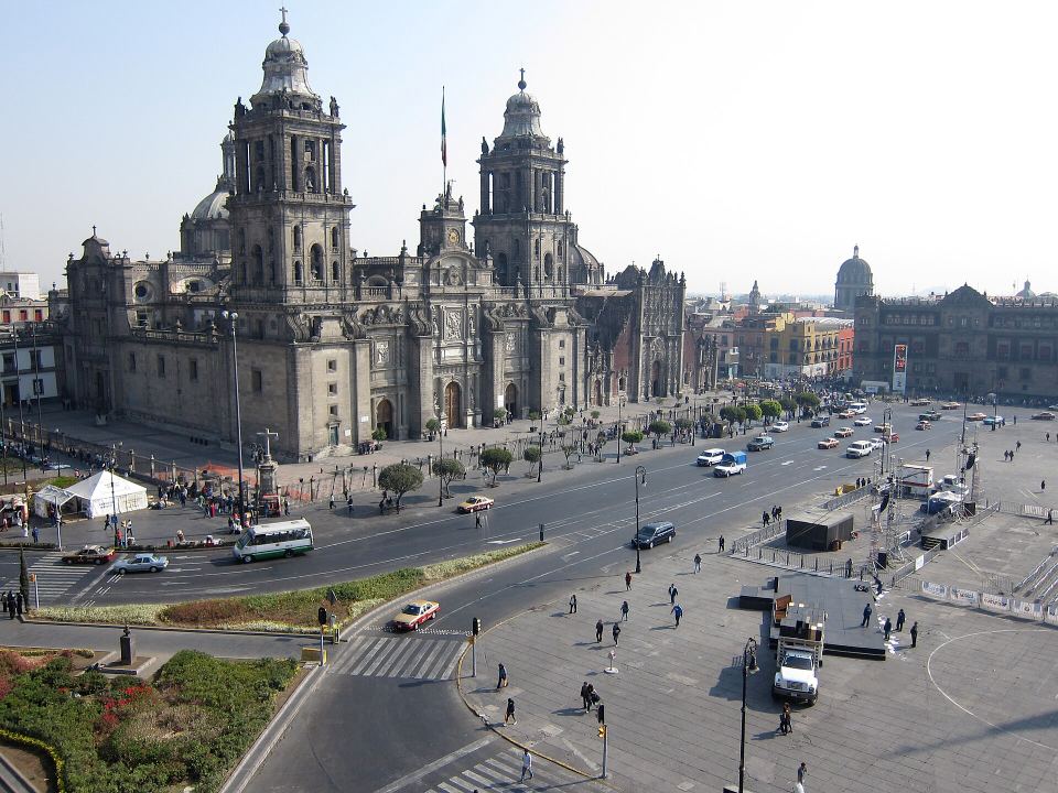 High-angle view of a massive stone cathedral beside a wide city square with cars.
