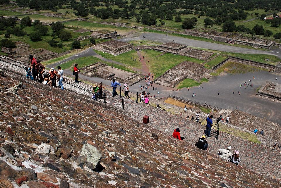 Tourists climbing down steep stone steps on a massive ancient pyramid.