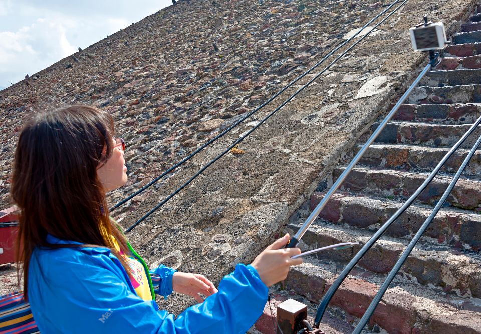 Side profile of a woman using a selfie stick while standing on stone pyramid steps.