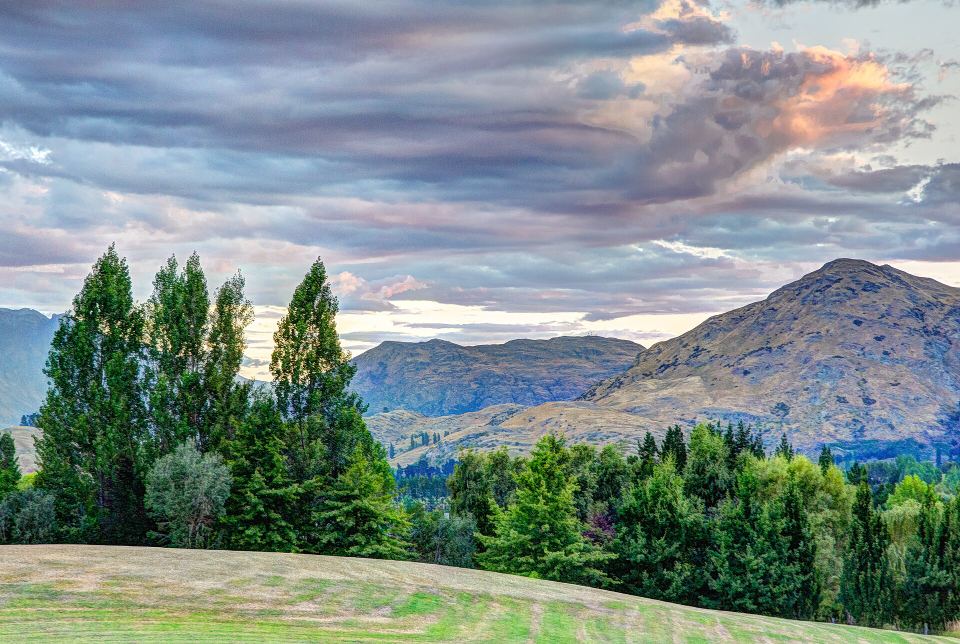 Soft sunset light over pine trees and rolling mountain hills under colorful clouds.