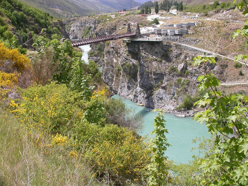 A historic suspension bridge spanning a deep canyon over a vibrant turquoise river.
