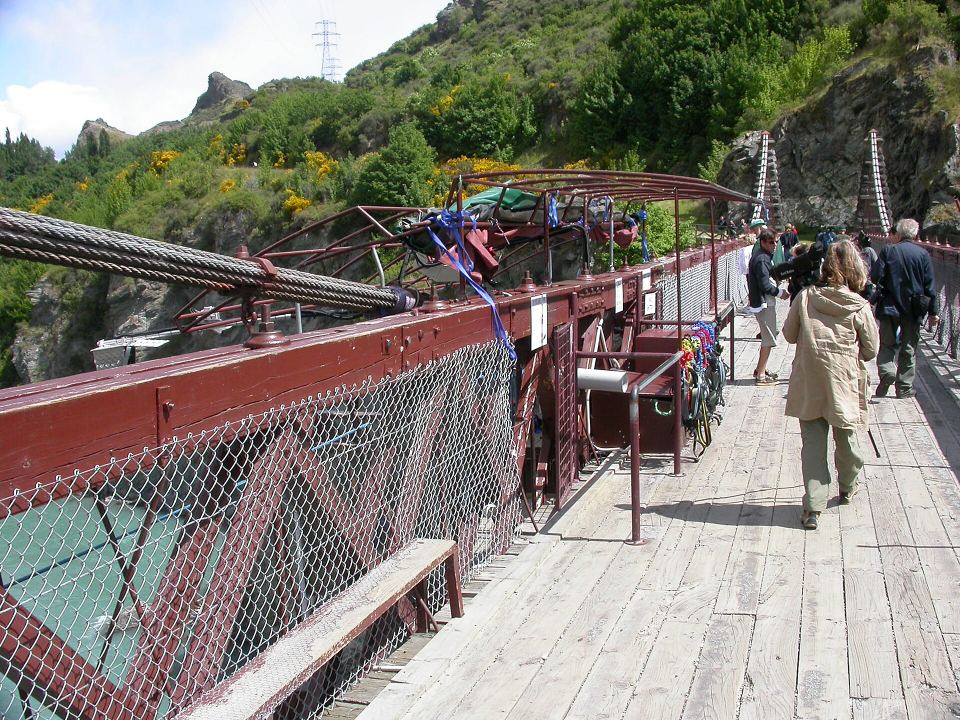 Wooden deck of a historic suspension bridge with tourists walking across.