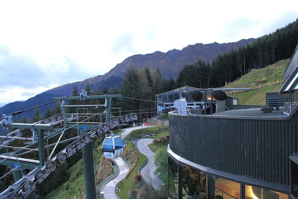 Skyline gondola cabins climbing above forest over Queenstown.