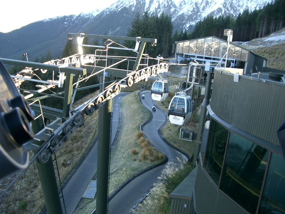 Gondola cabins suspended on cables above a winding luge track built on a mountain slope.