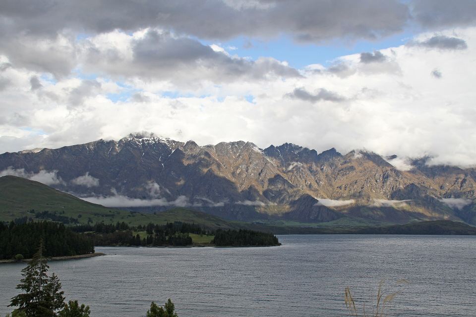 Mountain range rising behind a dark blue lake under dramatic gray and white clouds.