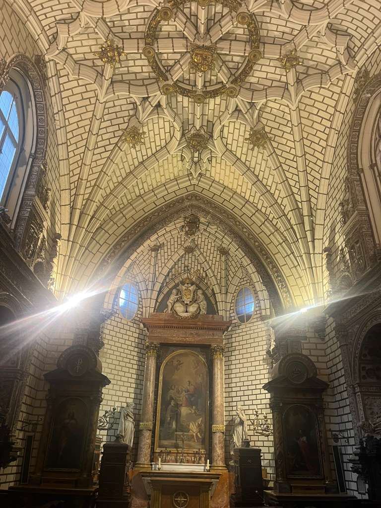 Vaulted church interior with brick-patterned arches looking toward a illuminated altar painting.