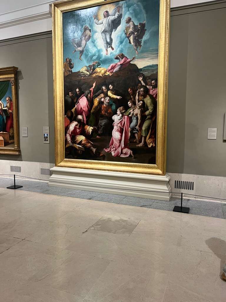 Framed Renaissance painting showing figures looking up toward a glowing figure in the sky.