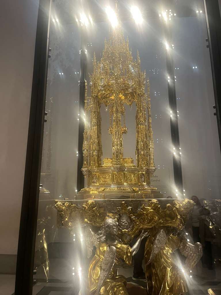 An intricate golden monstrance tower displayed inside a glass case in a dimly lit museum.