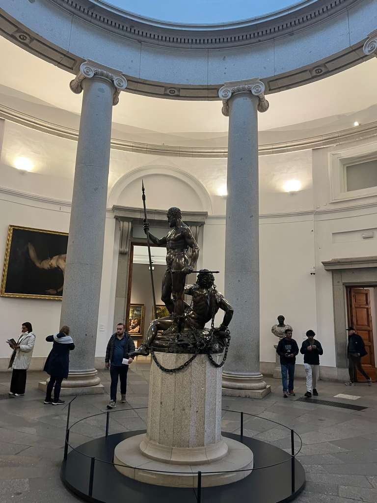 Classical bronze statues centered in a circular gallery supported by tall stone columns.