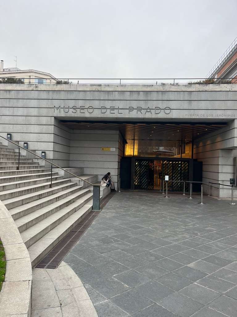 Modern stone entrance to the Museo del Prado with wide stairs leading down to glass doors.
