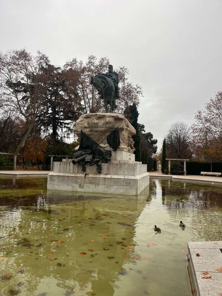 A bronze statue of a rider on horseback in the center of a pond surrounded by autumn leaves.