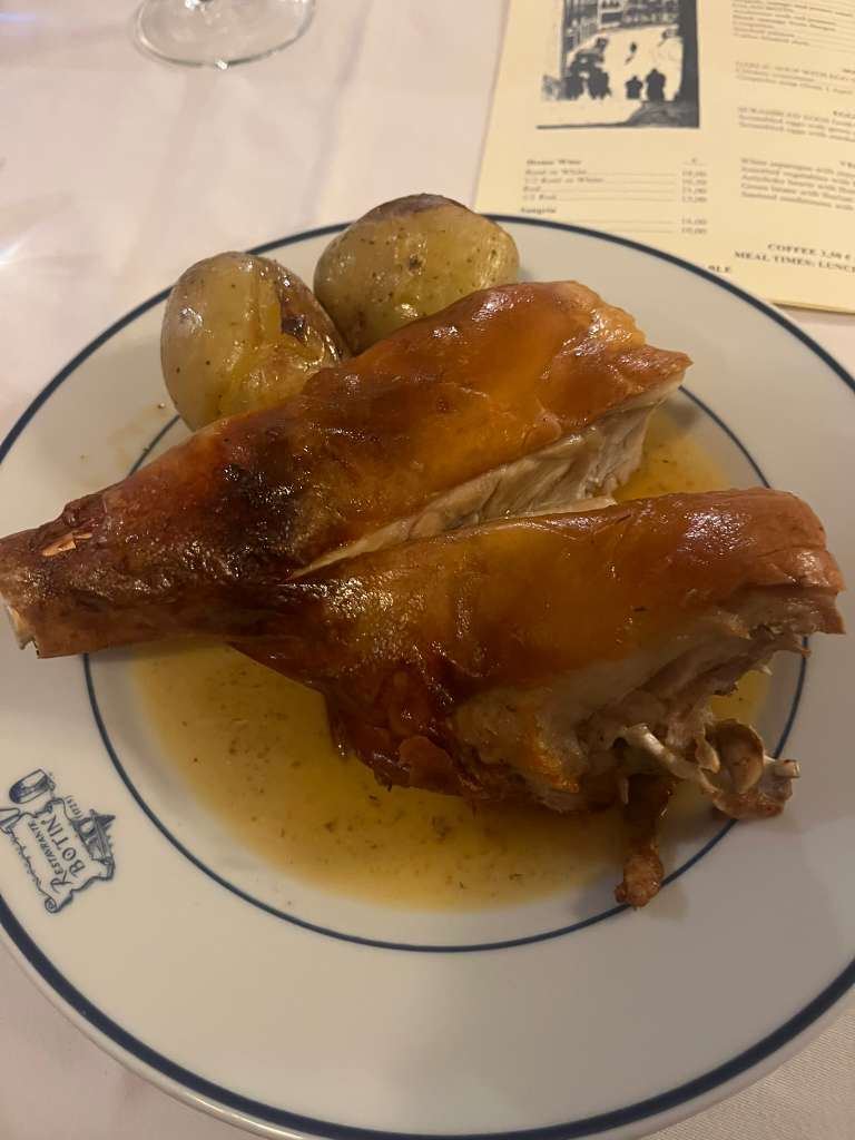 Plate of crispy roasted suckling pig with potatoes on a branded white plate beside a menu.