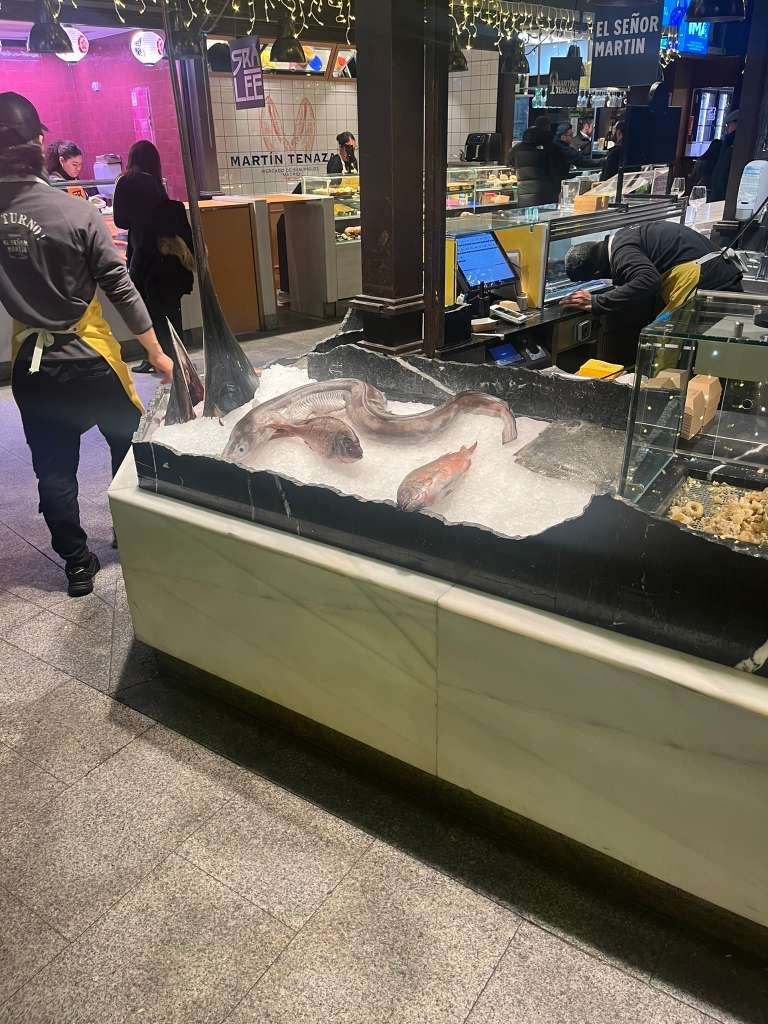 Fresh seafood arranged on crushed ice at an indoor food market counter.