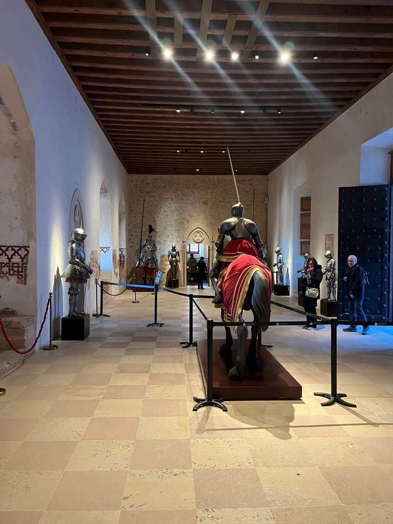Suits of plate armor on display along a grand historic hall with a wooden beam ceiling.