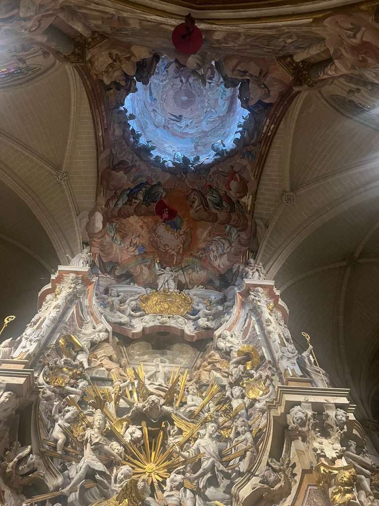 Intricate Baroque altarpiece with sculpted figures bathed in sunlight from an overhead dome.
