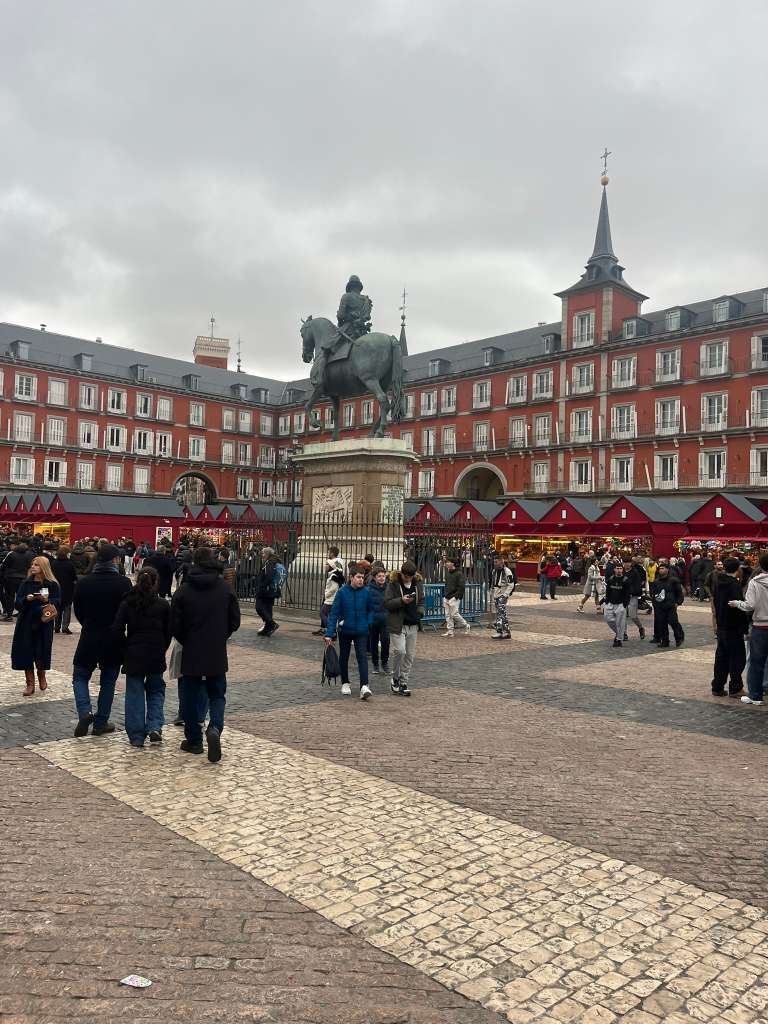 Crowded historic square enclosed by red buildings with an equestrian statue at its center.