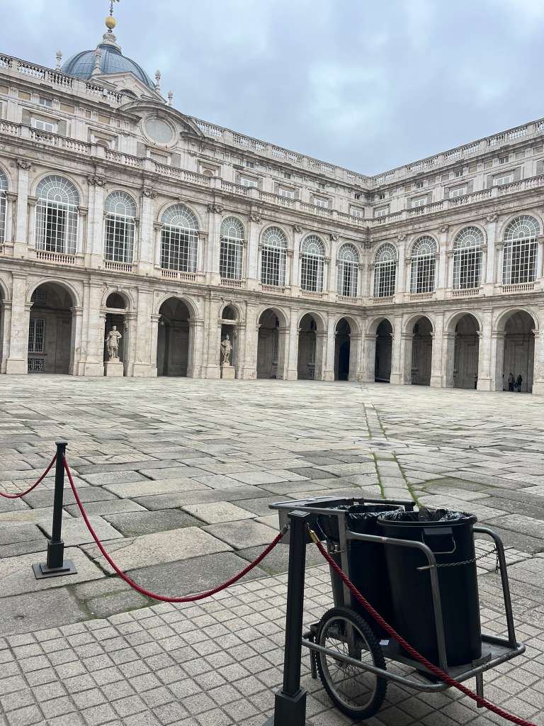 Grand stone courtyard surrounded by multi-tiered arched palace walls under a cloudy sky.