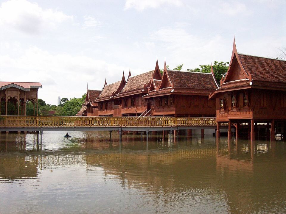 A red-roofed Thai timber pavilion standing on stilts over water at Ancient City, Samut Prakan