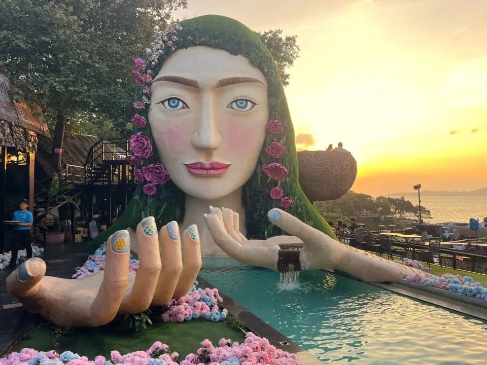The Three Mermaids statue in Pattaya at sunset, its cupped hands reaching over a pool of water